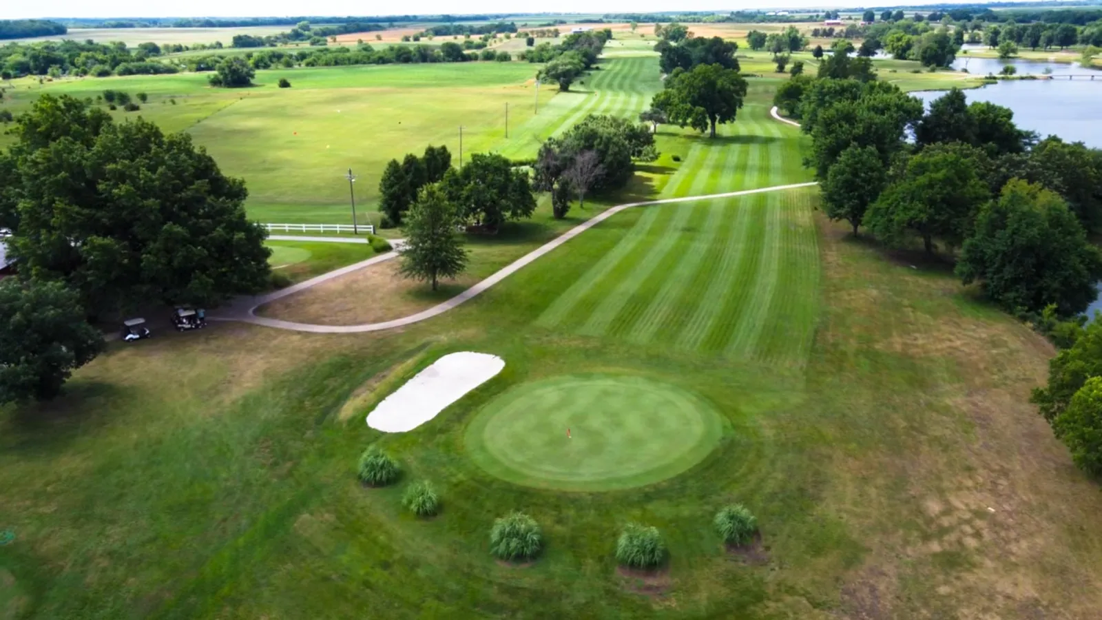 A manicured green and sand bunker on the Osage City Golf Course, fairway leading toward the lake