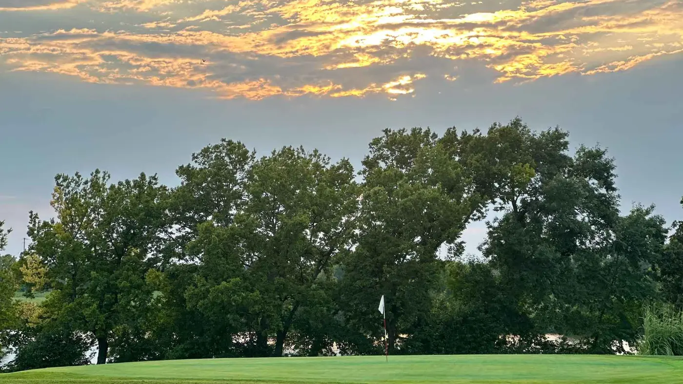 Evening light over a green at Osage City Golf Course, with mature trees and the lake beyond.