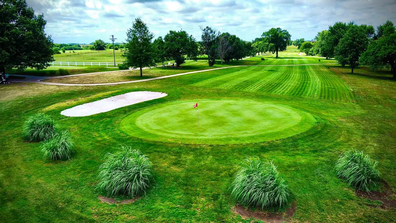 The practice putting green at Osage City Golf Course, framed by ornamental grasses with the fairway beyond